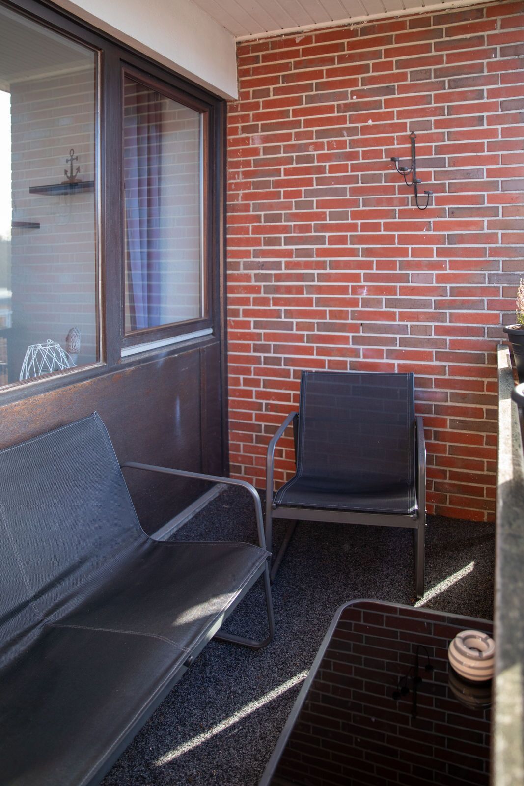 A small outdoor seating area with a brick wall, a window, and a metal chair.