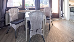 Comedor con sillas de mimbre y una mesa, un radiador y vistas al exterior a través de amplios ventanales.