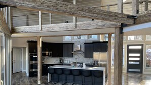 A modern kitchen with a central island, black bar stools, and a stainless steel refrigerator.