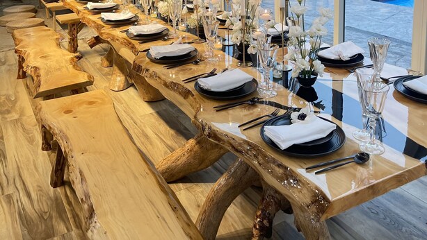 A long wooden dining table set with white flowers, candles, and glassware, overlooking a pool area.