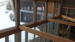 A multi-level interior with large windows, wooden beams, and a view of a snowy outdoor area.