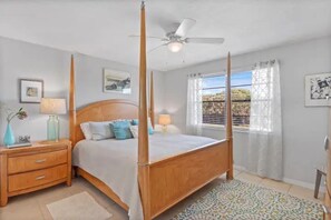 Una cama con dosel y tablero de madera, una mesita de noche con lámpara, y una ventana con cortinas.