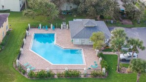 Uma piscina com formato geométrico, cercada por um deck pavimentado e espreguiçadeiras.