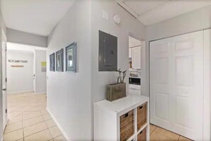 A hallway with a white door, a white console table with baskets, and a kitchen area in the background. - Topsail at Schooner Court (St. Augustine Beach)