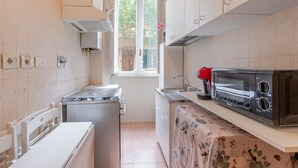 A compact kitchen with white cabinets, a built-in stove, a toaster, and a window providing natural light.