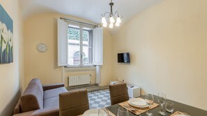 A dining area with a table set for four, a sofa, and a window with shutters.