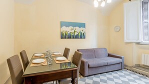 A dining area with a table set for four, a sofa, a painting on the wall, and a clock.