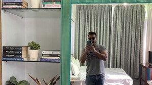Ett hotellrum med en säng, en spegel, en bokhylla med böcker och krukväxter.