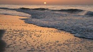 Ein Strand bei Sonnenuntergang, wobei Wellen auf das Ufer zurollen.