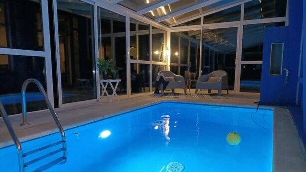 Une piscine intérieure avec des parois en verre transparent, une échelle et quelques chaises longues.