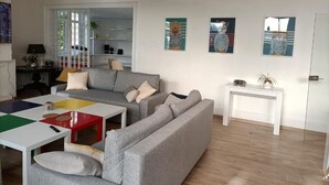 Un salon moderne avec un canapé gris, une table basse colorée et une table d’appoint blanche. Trois œuvres d’art encadrées ornent le mur.