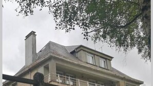 Une maison à deux étages avec un balcon, une cheminée et un mur de pierre au premier plan.
