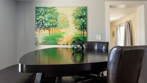 Un comedor con una mesa redonda, sillas y un cuadro que muestra un camino bordeado de árboles.