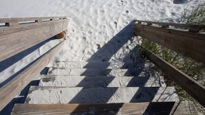 Una escalera de madera que baja a una playa de arena.