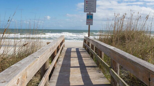 Un muelle de madera que conduce a la playa, con indicaciones de acceso a la playa y una estación de salvavidas.