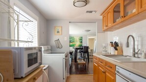 Cocina compacta con microondas, horno y lavabo. Se aprecia un comedor con mesa y sillas al fondo.