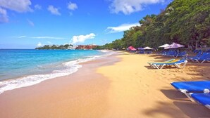Une plage avec une eau d’un bleu limpide, un rivage sablonneux et des chaises longues bleues.