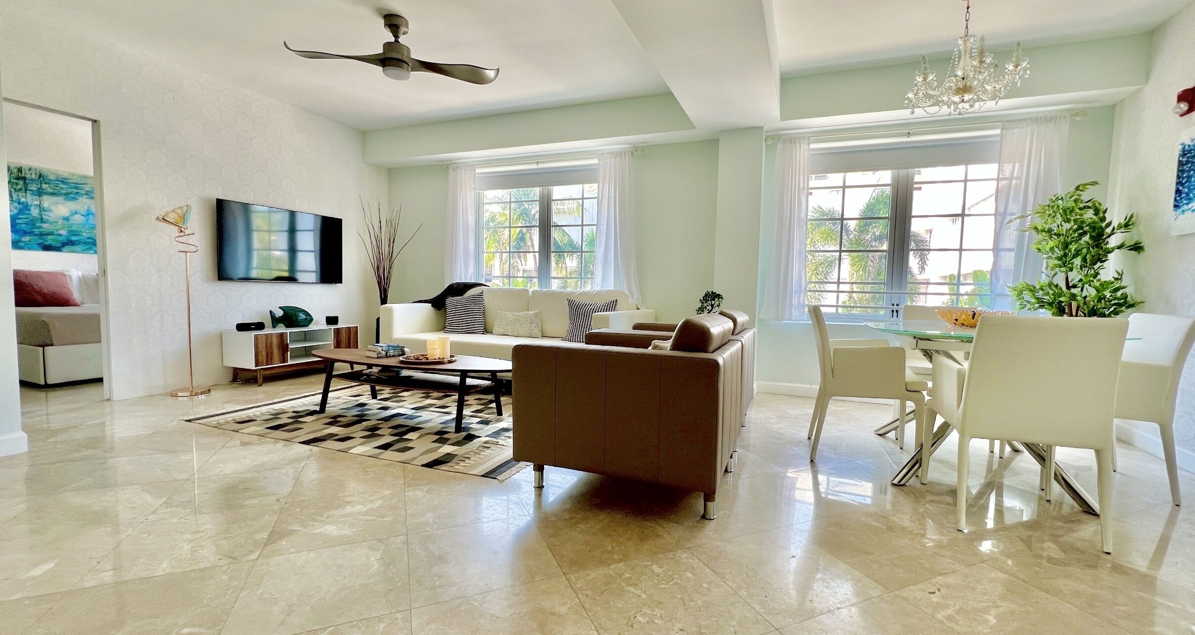A spacious living room with a large sofa, a dining area with white chairs, and a ceiling fan.