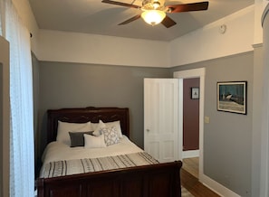 A bedroom with a wooden bed, a ceiling fan, and a door leading to another room.