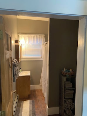 A narrow bathroom with a sink, window with blinds, and a towel rack.