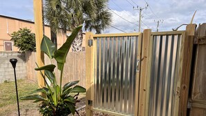 A wooden deck with a potted plant, a metal gate, and a wall with a number sign.
