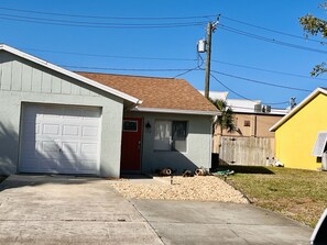 A single-story house with a garage, a red door, and a small front yard with gravel and a palm tree. - JUST BEACHY A Seaside Serenity Coastal Retreat Outdoor Shower FastWifi  (Indialantic)