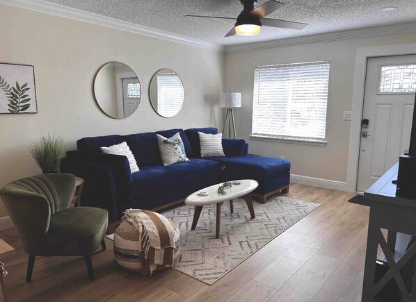 A living room with a blue sofa, two round mirrors, a small white table, and a floor lamp. - JUST BEACHY A Seaside Serenity Coastal Retreat Outdoor Shower FastWifi  (Indialantic)