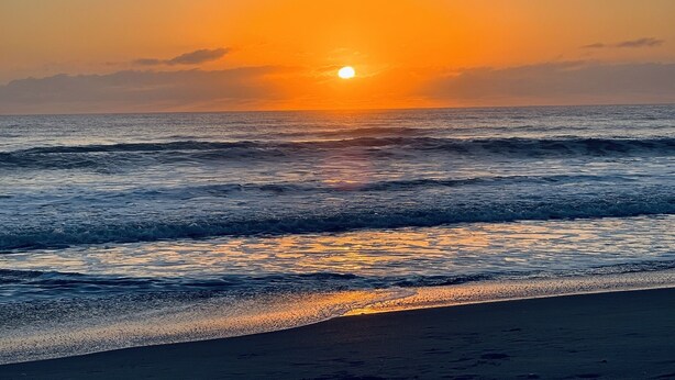 A sunset over the ocean with waves approaching the shore.