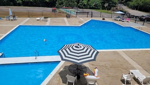 Een zwembad met een zwart-wit gestreepte parasol, witte ligbedden en een kleine tafel met een stoel.