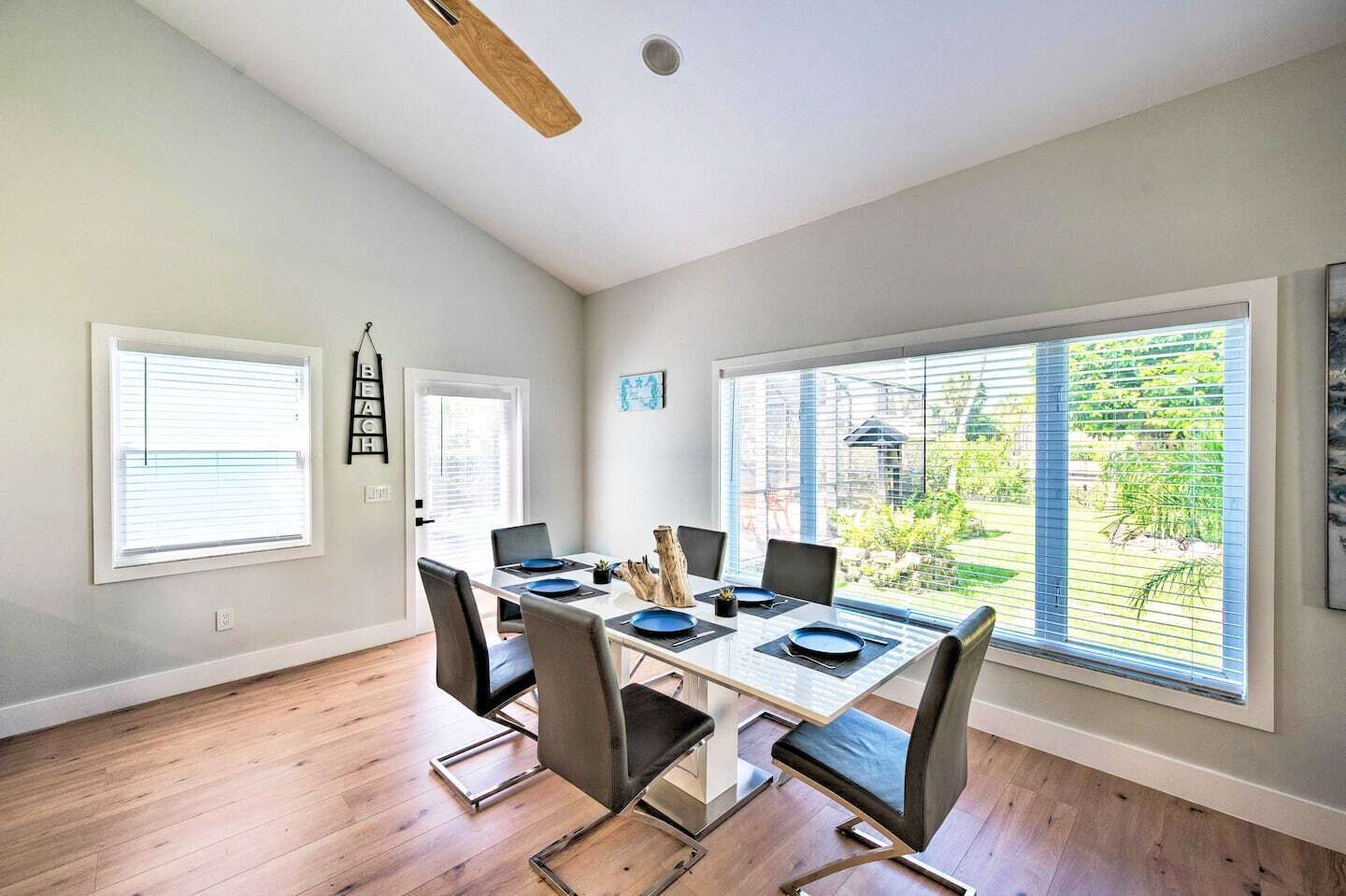 A dining area with a wooden table, six chairs, and a view of a garden through large windows.