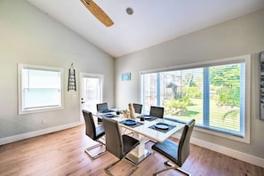 A dining area with a wooden table, six chairs, and a view of a garden through large windows. - NEW! Clean, Cozy Beach home w/Ocean Access, 5Mi to Beach (Bonita Springs)