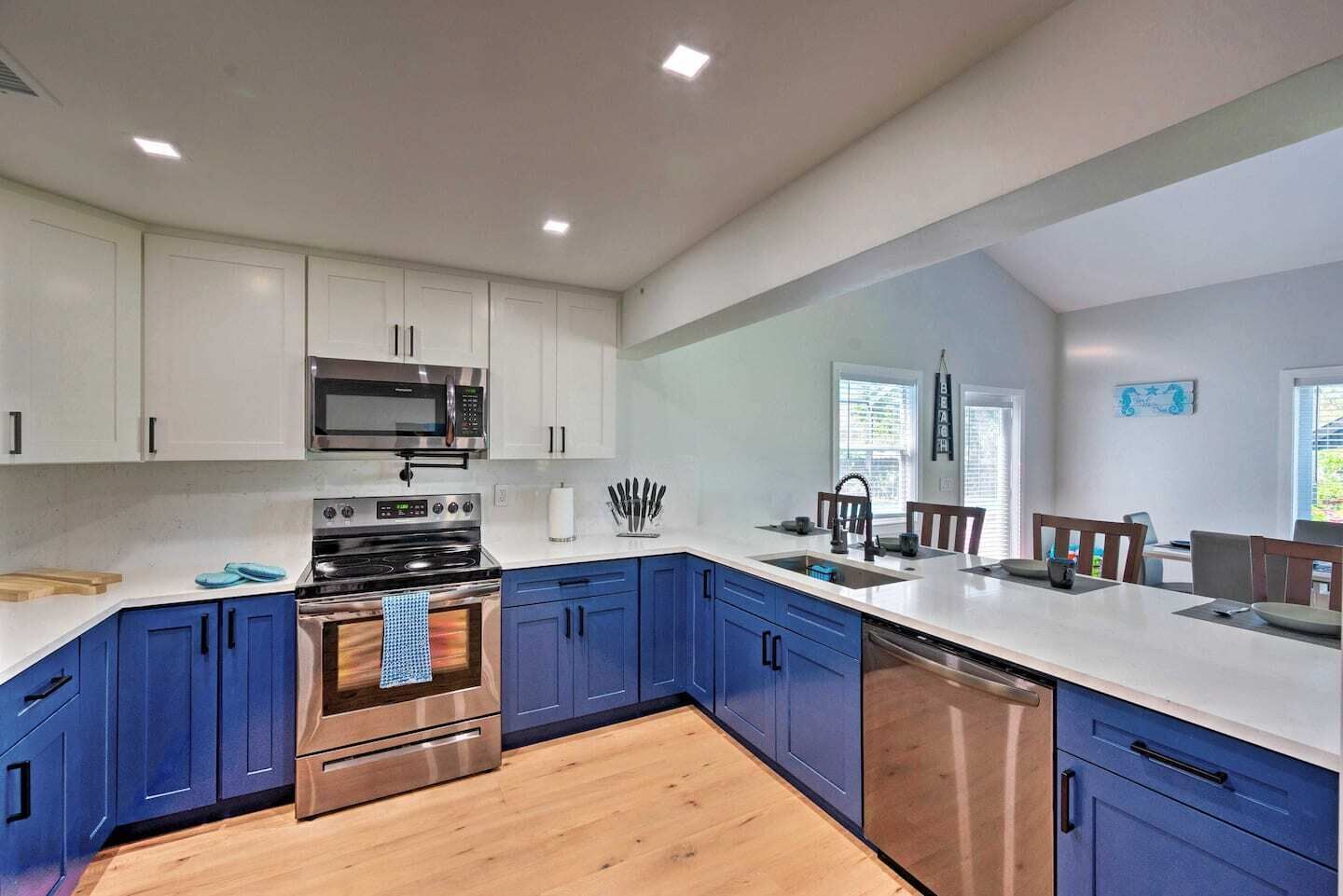 A modern kitchen with white upper cabinets, blue lower cabinets, stainless steel appliances, and a wooden floor.