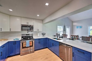 A modern kitchen with white upper cabinets, blue lower cabinets, stainless steel appliances, and a wooden floor. - NEW! Clean, Cozy Beach home w/Ocean Access, 5Mi to Beach (Bonita Springs)