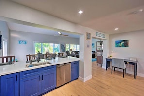 A modern kitchen with blue cabinets, a dishwasher, and a dining area with a table and chairs. - NEW! Clean, Cozy Beach home w/Ocean Access, 5Mi to Beach (Bonita Springs)