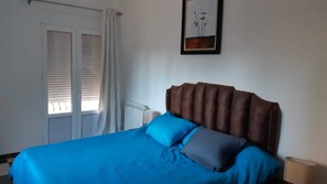 A bedroom with a large bed, a headboard, a window with blinds, and a framed picture on the wall.