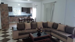A living room with a sectional sofa, a coffee table, and a dining area with a table and chairs. - Apartment in perfect condition sea view (Rais Hamidou)