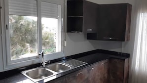 A kitchen with a double sink, dark cabinets, and a window with blinds. - Apartment in perfect condition sea view (Rais Hamidou)