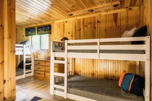 Interior de una cabaña de madera con literas, un escritorio y una ventana.