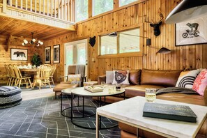 A wooden cabin interior with a dining area, a sofa, and a table with drinks.
