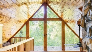A wooden interior with a large triangular window, a stone wall, and a wooden staircase. - 5BR/5BA Cabin, Sleeps 14, Hot Tub/Game Rm, Pool Close, 5min to G'burg/Nat'l Park (Gatlinburg)