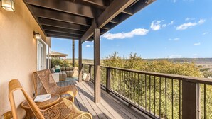 Ein überdachter Balkon mit Korbmöbeln, Blick auf die Landschaft und ein Holgitter.