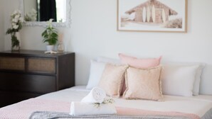 Une chambre à coucher avec un lit, des oreillers, une table de chevet, un miroir et un tableau encadré accroché au mur.