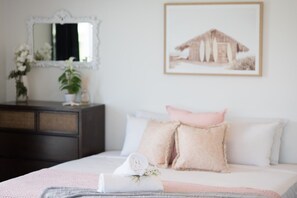 A bedroom with a bed, pillows, a bedside table, a mirror, and a framed picture on the wall. - Ocean Dreams On Airlie - Premiere (Airlie Beach)