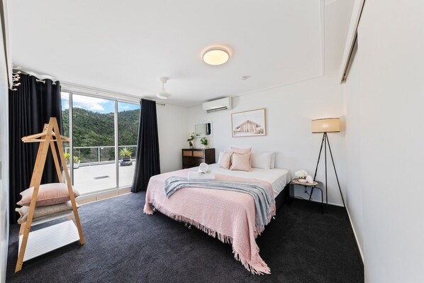 A hotel room with a bed, a bedside table, a lamp, a hanging chair, and a view of the outdoors.