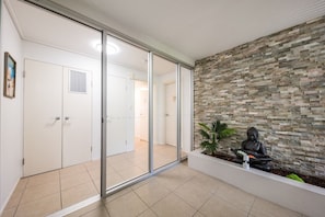A modern interior with a stone wall, a Buddha statue, and a sliding glass door leading to a room. - Ocean Dreams On Airlie - Premiere (Airlie Beach)