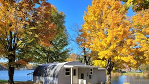 A small cabin by a lake with autumn foliage, a clear sky, and a calm water body. - Lakeside Quonset Hut, Cozy And Romantic (Paw Paw)