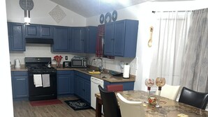 Uma cozinha com armários azuis, fogão, micro-ondas e uma área de jantar com mesa e cadeiras.