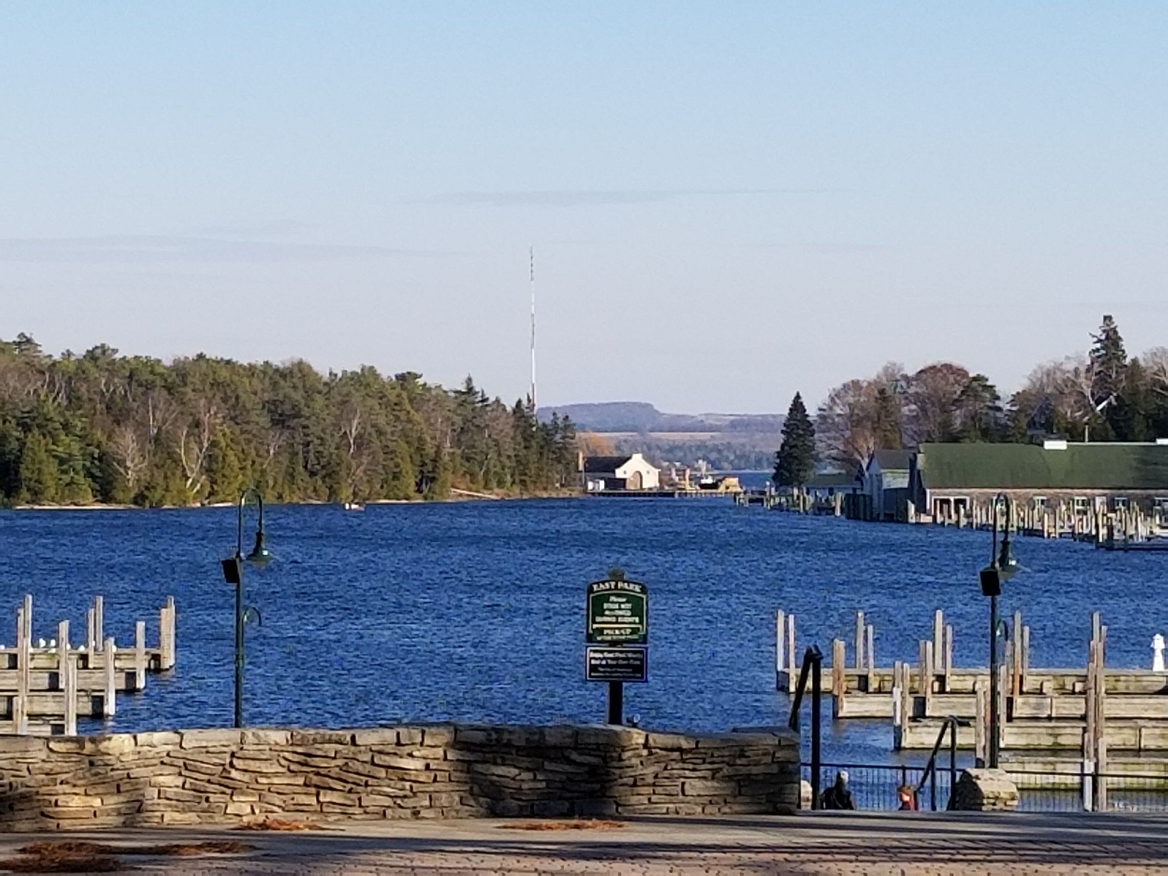 A waterfront view with a stone wall, wooden dock, and a sign indicating a public area.
