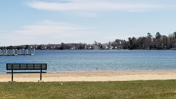 A bench on a grassy area by a calm lake with a dock in the background. - Winter Ski Holiday at Boyne Mountain - Cozy Luxury Villa (Boyne Falls)