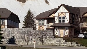 A two-story house with a stone foundation and a sloped roof, situated on a hillside with a ski lift in the background. - Winter Ski Holiday at Boyne Mountain - Cozy Luxury Villa (Boyne Falls)